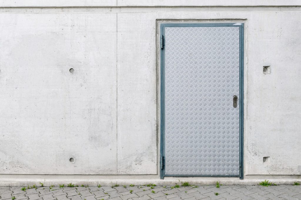 Concrete building wall facade with armored steel diamondplate textured door. Undeground safety